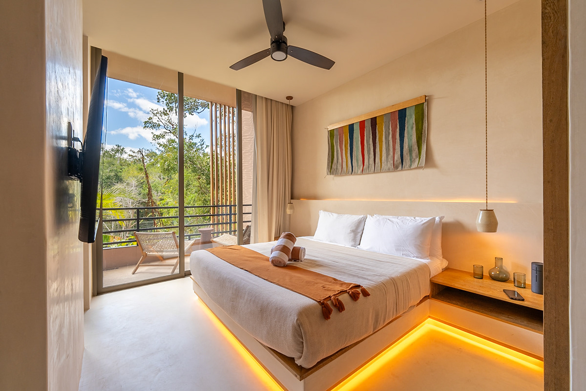 Studio bedroom with warm under-bed lighting and a balcony framed by trees — Aflora 214